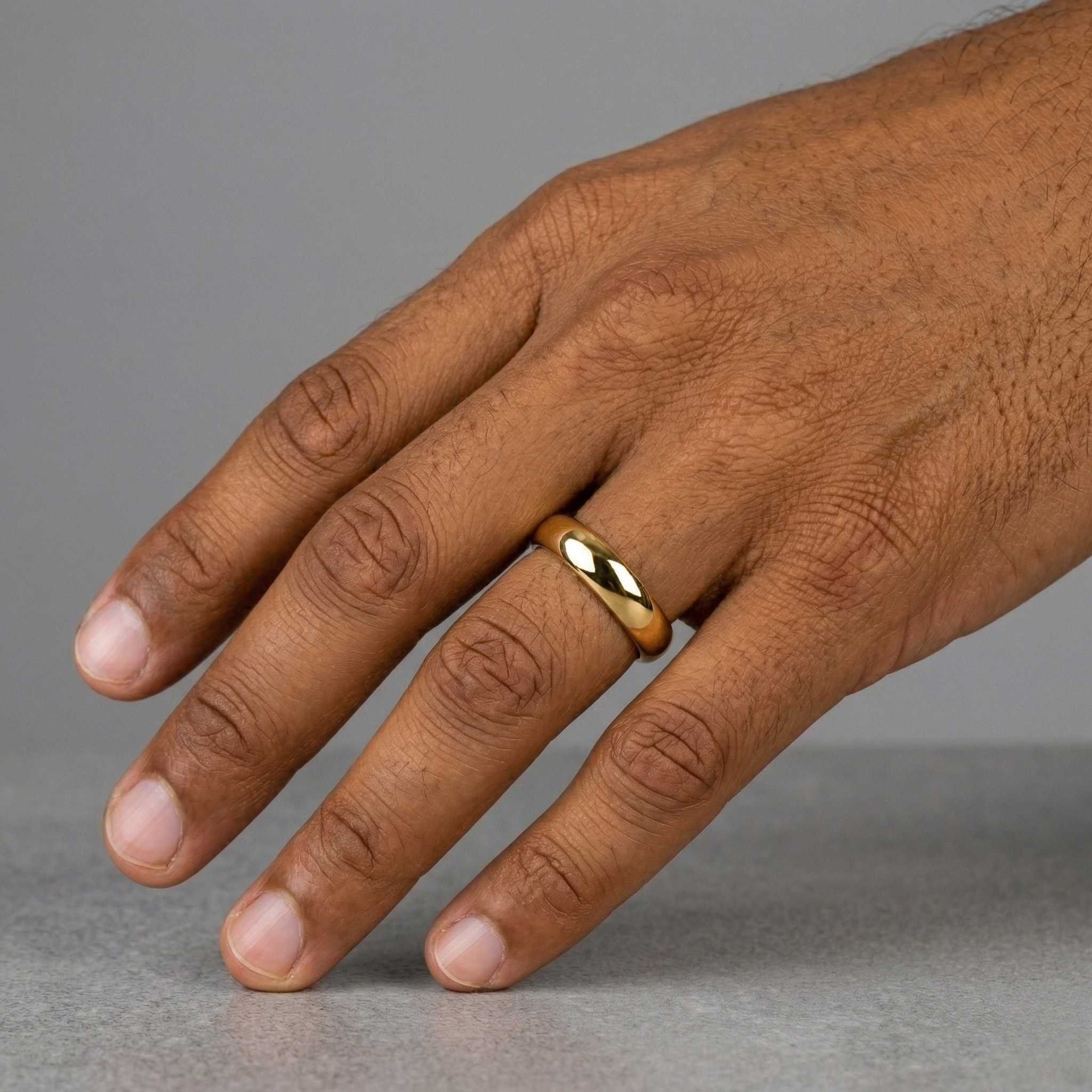 Hand wearing a gold ring on a gray background