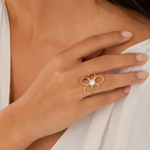 Gold orchid-style ring with a central gemstone on a model's hand, showcasing floral design elegance.