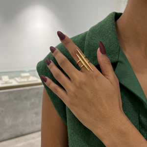 Gold split pillar ring on woman's hand with burgundy nails, wearing a green vest in a jewelry store setting