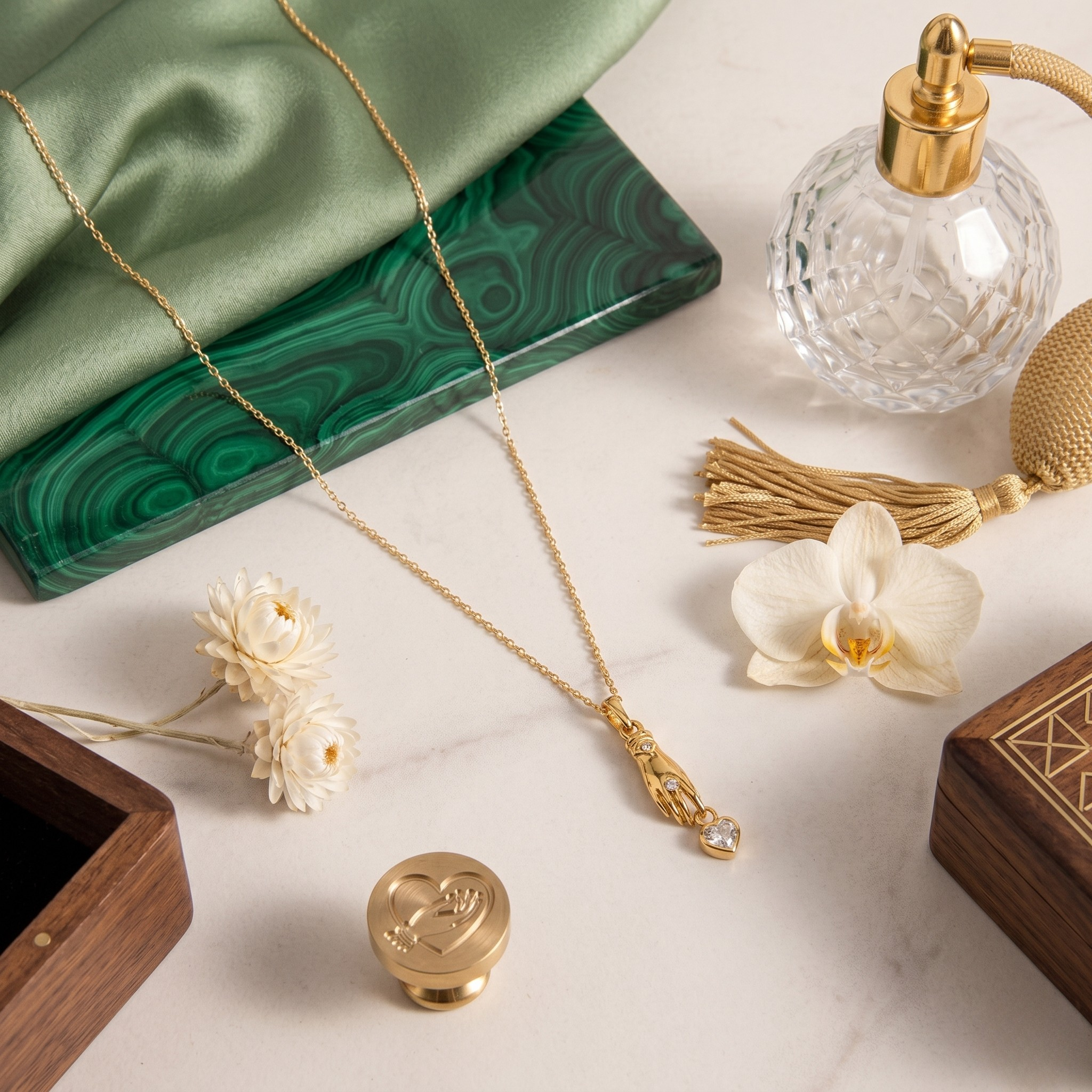 Gold heart stone charm pendant on a chain, displayed with flowers and perfume bottle on a marble surface.