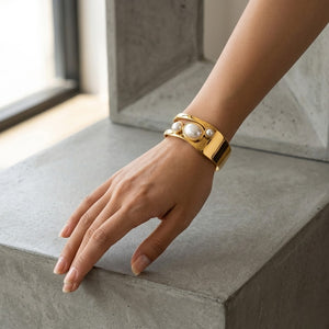 Gold cuff bracelet with pearls worn on a wrist, casual setting, modern style.