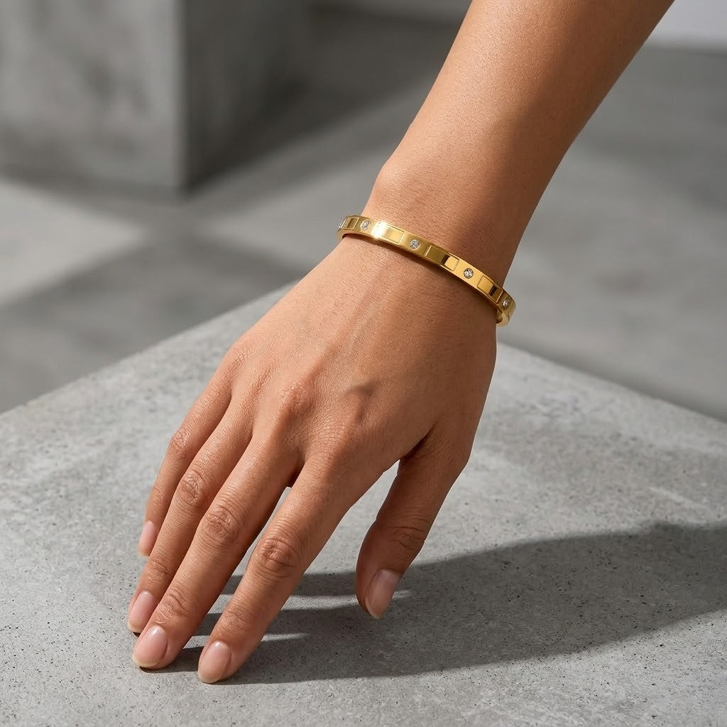 Gold banded metal cuff on wrist, minimalist style, resting on a concrete surface.