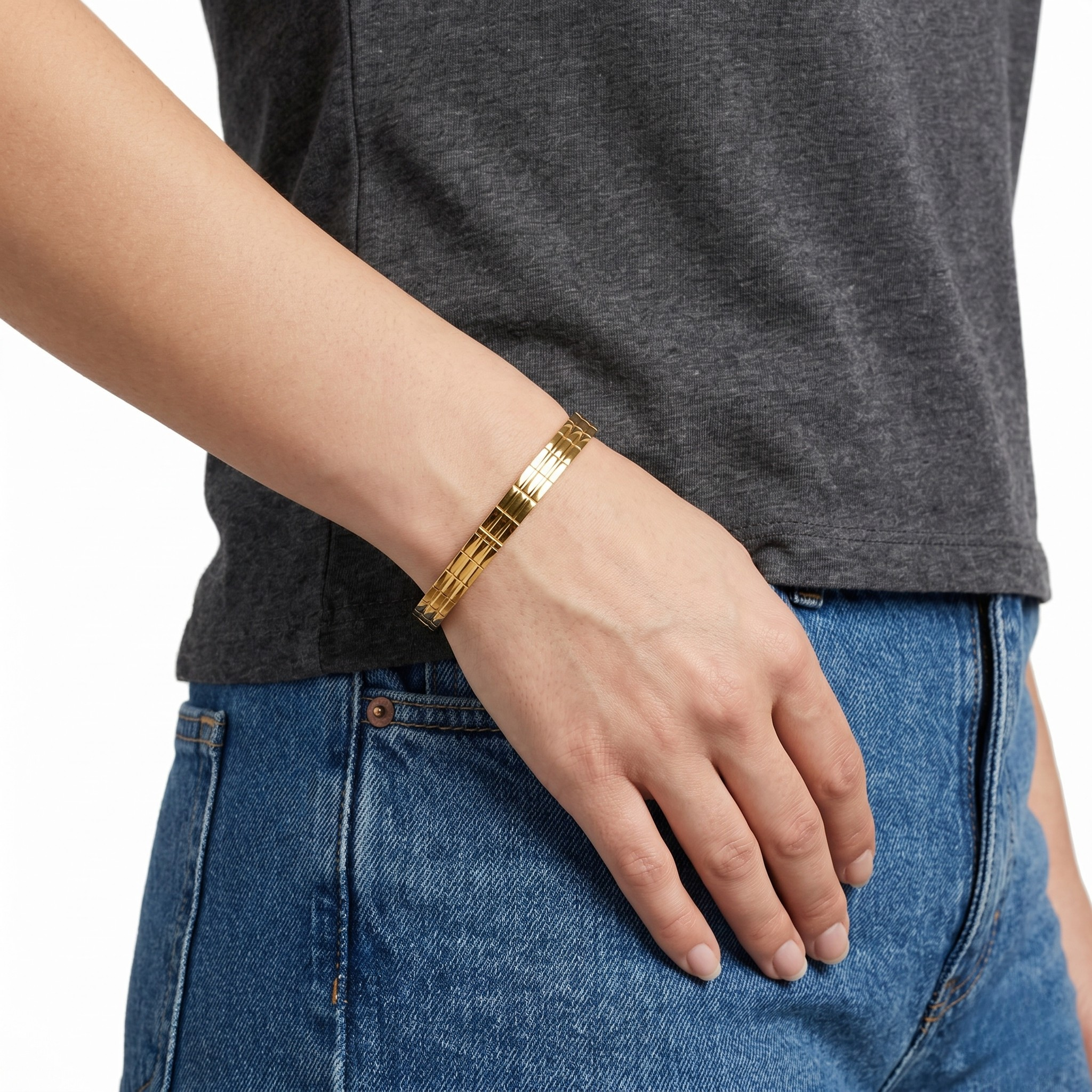 Gilded gold bracelet worn on wrist, paired with gray shirt and blue jeans for casual style look