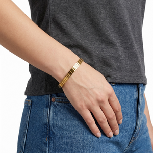 Gilded gold bracelet worn on wrist, paired with gray shirt and blue jeans for casual style look