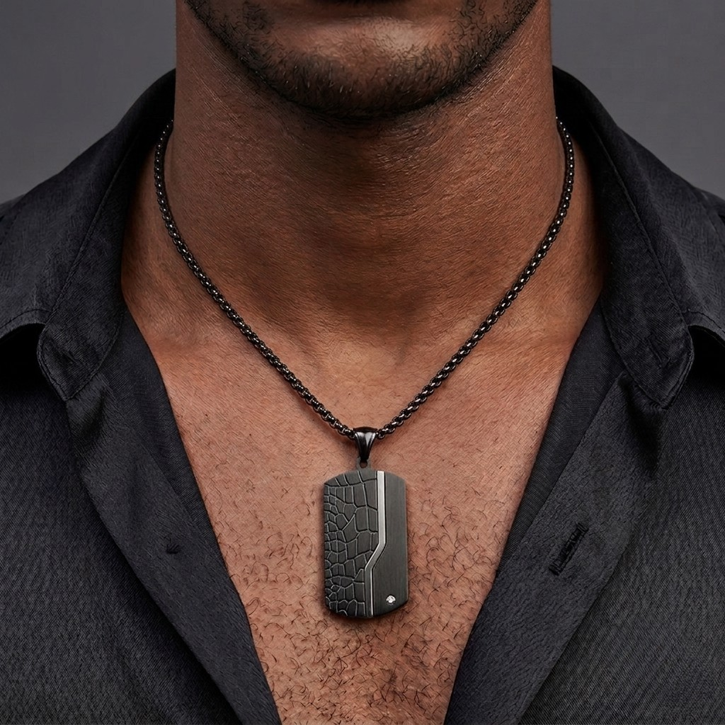 A close-up of a man's neck and chest wearing a dark textured rectangular pendant necklace on a black chain, over a dark open-collar shirt.