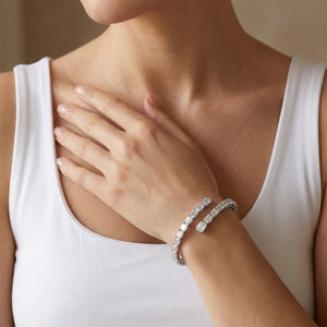 Flexible sterling silver open wrap tennis bracelet set with emerald-cut cubic Moissanite crystals worn on wrist by model Tiffany wearing a white tank top by J.Collins

