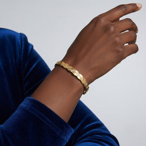 Gold bracelet on a wrist with a blue sleeve against a light gray background