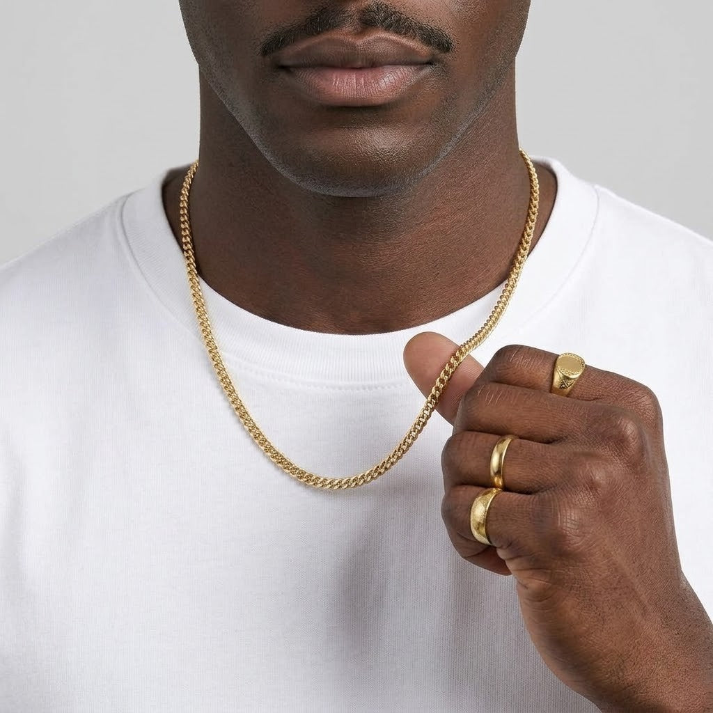 A close-up of a man wearing a gold chain necklace and gold rings, wearing a white t-shirt against a light gray background - J.Collins Jewelry