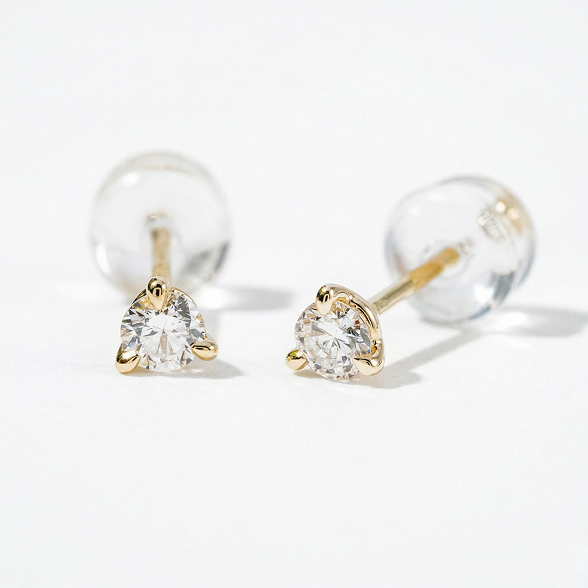 Pair of gold earrings with clear gemstones on a light gray background - Diamond Earrings Martini 0.1ct - J Collins Jewelry 