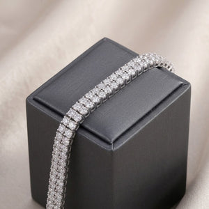 Double-row sterling silver tennis bracelet set with round cubic Moissanite crystals draped over a dark grey jewelry box by J.Collins
