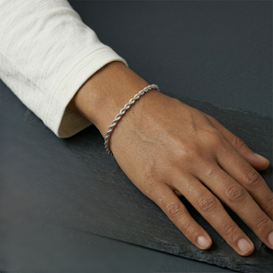 Hand wearing a silver bracelet on a dark surface-J.Collins Jewelry