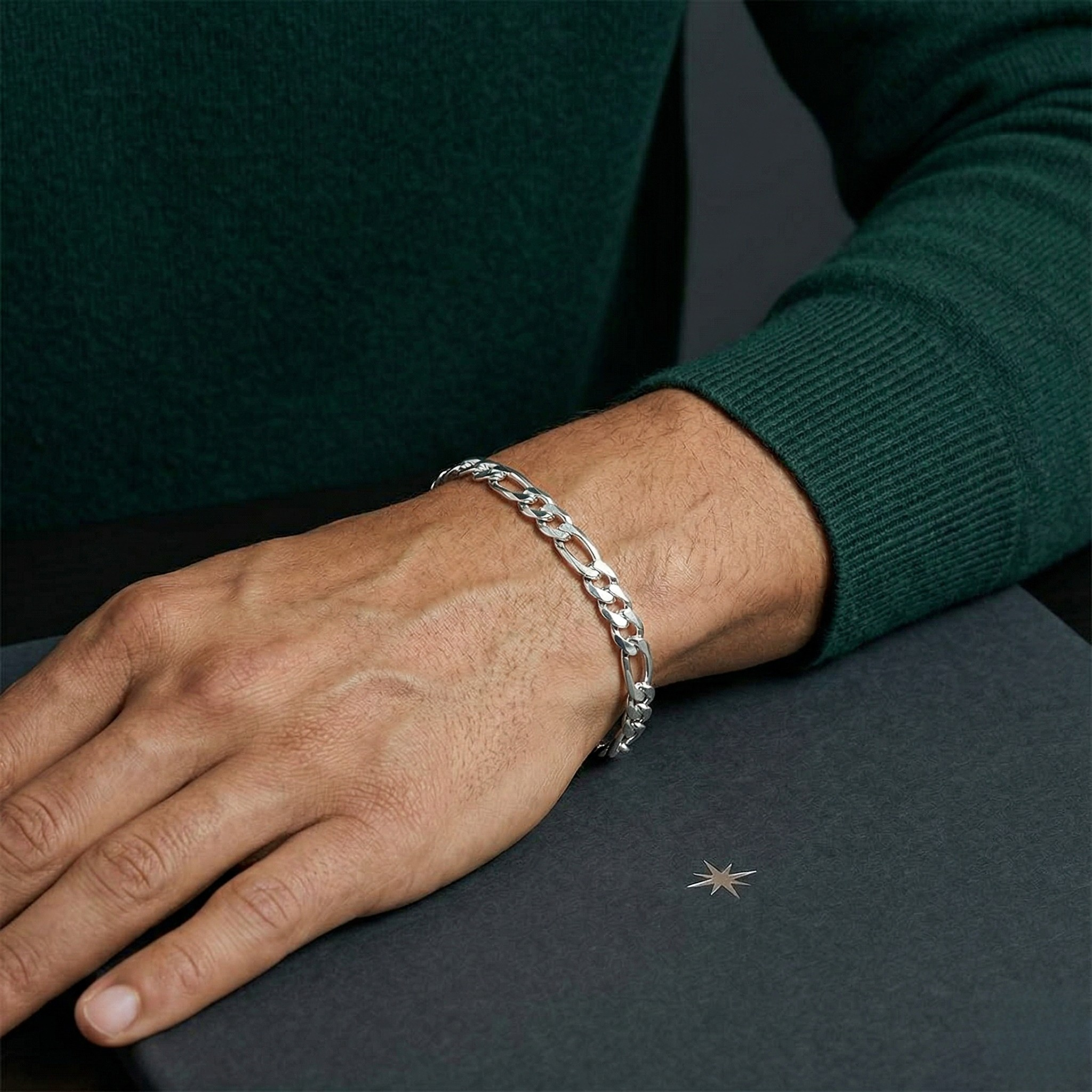 Silver bracelet on a person's wrist with a dark green sweater and gray surface-J.Collins Jewelry
