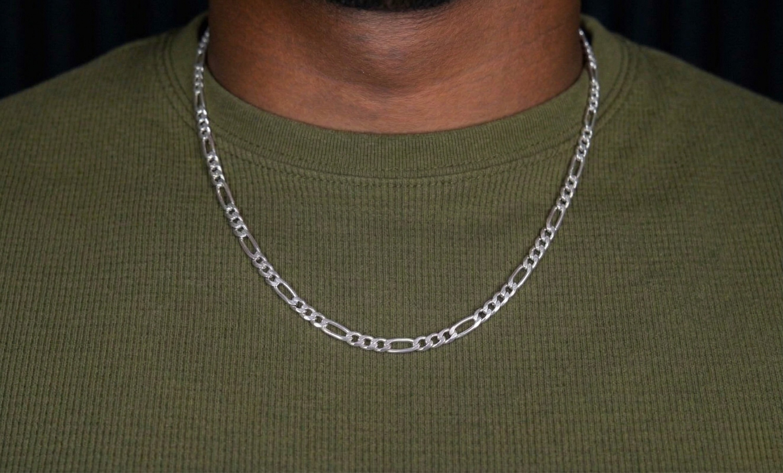 Silver chain necklace on a person wearing a green shirt against a dark background-J.Collins Jewelry