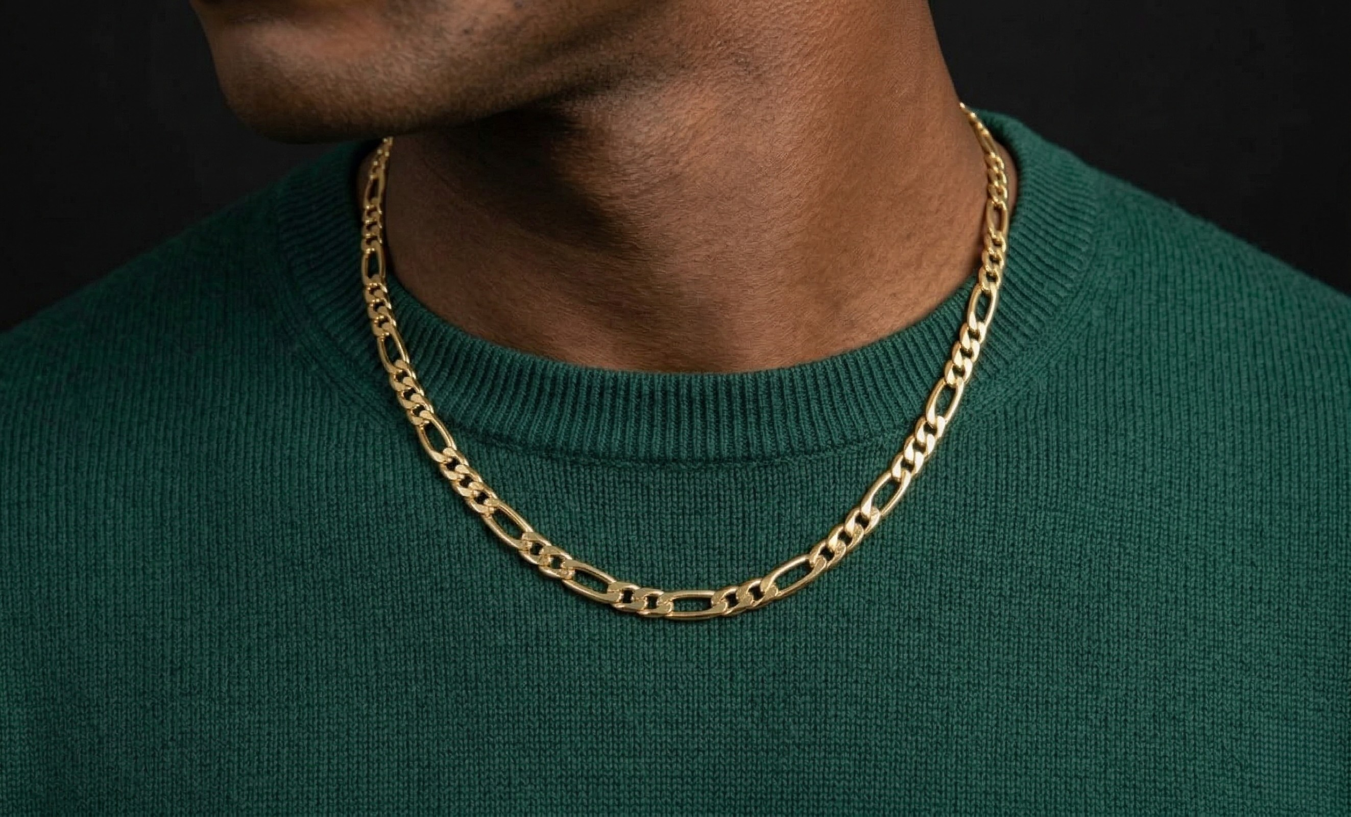 Gold chain necklace worn by a person in a green sweater against a black background-J.Collins Jewelry