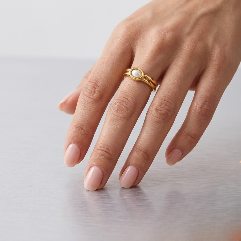 Hand wearing a gold ring with an inset gemstone on a light surface, showcasing elegant style and design.