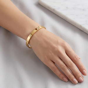 Gold Bangle bracelet on wrist, simple elegant design, displayed on light fabric surface.