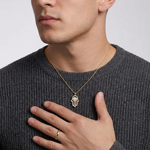 Gold Hamsa hand pendant necklace set with pave moissanite and a round center stone worn around neck by model wearing a dark grey crewneck sweater by J.Collins
