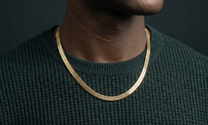 Gold herringbone necklace worn by a person against a dark background-J.Collins Jewelry