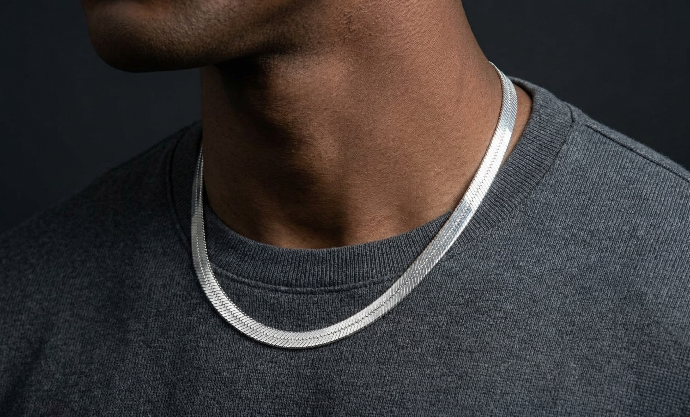 Close-up of a person wearing a silver herringbone necklace against a dark background-J.Collins Jewerly