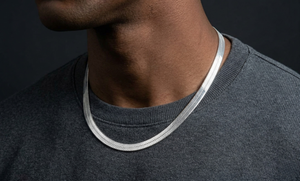 Close-up of a person wearing a silver herringbone necklace against a dark background-J.Collins Jewerly