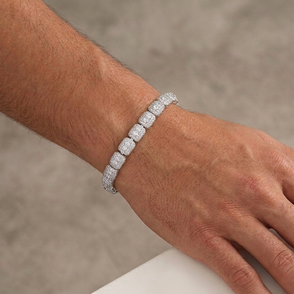 A close-up photograph of a white gold iced-out tennis bracelet featuring cushion-cut cluster links, worn on a male model's wrist against a textured grey background - J.Collins Jewelry
