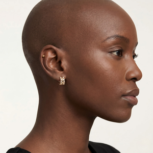 Close-up of a woman wearing gold earrings on a plain background-J.Collins Jewelry