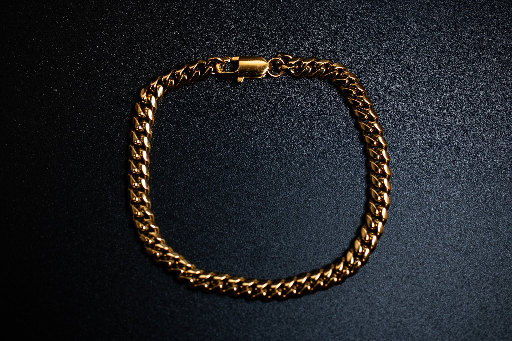 Gold chain bracelet on a dark background-Iconic-Cuban-Bracelet-JCollins-Jewelry