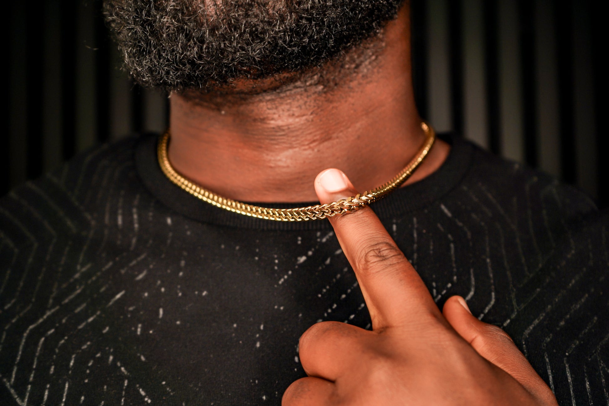 Person wearing a gold chain necklace with a finger pointing to it against a dark background -Signature-Franco-Chain-JCollins-Jewelry