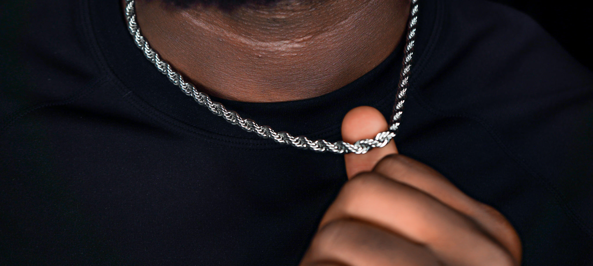 Close-up of a silver chain necklace held by a person against a dark -Essential-Rope-Chain-JCollins-Jewelry 