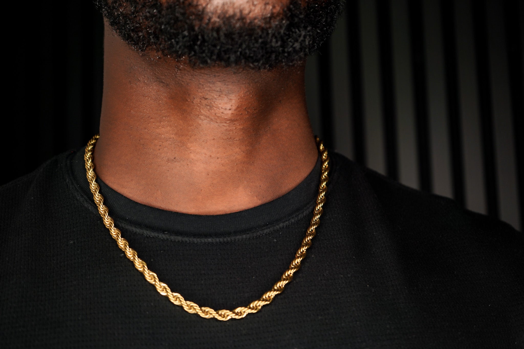 Gold chain necklace on a person wearing a black shirt against a dark background-J.Collins Jewelry