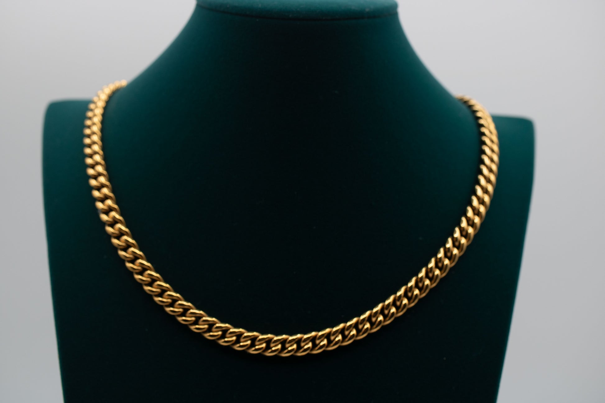 Gold chain necklace on a green mannequin bust against a gray background-Iconic-Cuban-Chain-JCollins-Jewelry