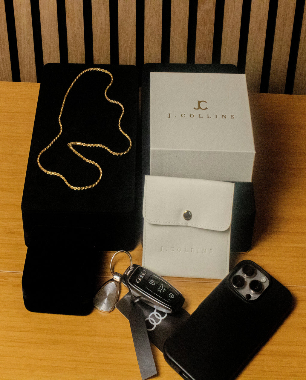 J. Collins jewelry box with gold chain, car keys, and phone on a wooden surface