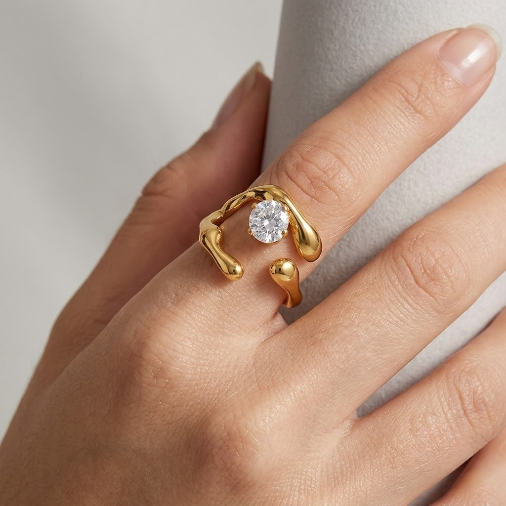 A gold ring with a round clear gemstone and organic, flowing open settings, shown worn on a hand against a soft light gray background -  J.Collins Jewelry