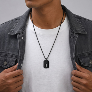 Person wearing a black dog tag necklace with a gray jacket and white shirt-J.Collins Jewelry
