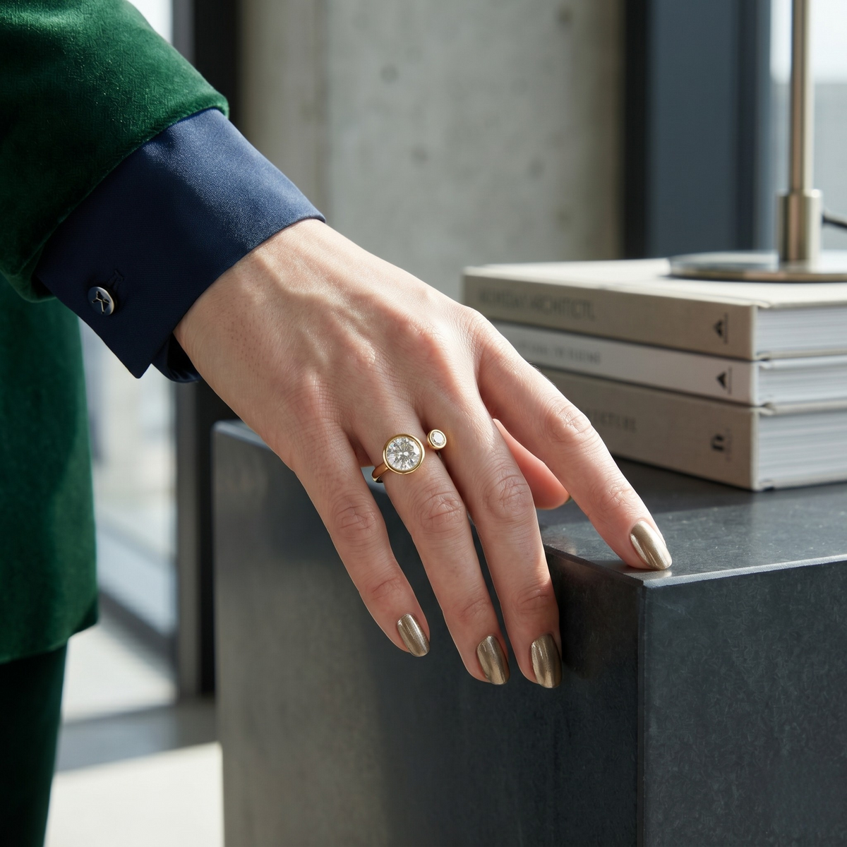 Open steel ring with a large clear gemstone and small gold accent on hand, next to stacked books in a modern setting - J.Collins Jewelry