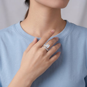 A close-up of a person wearing a silver ring with a square-cut clear gemstone, styled with a matching silver band, while wearing a light blue crewneck t-shirt - J.Collins Jewery