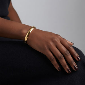 Hand wearing a gold bracelet on a dark surface with a gray background. J.Collins Jewelry 