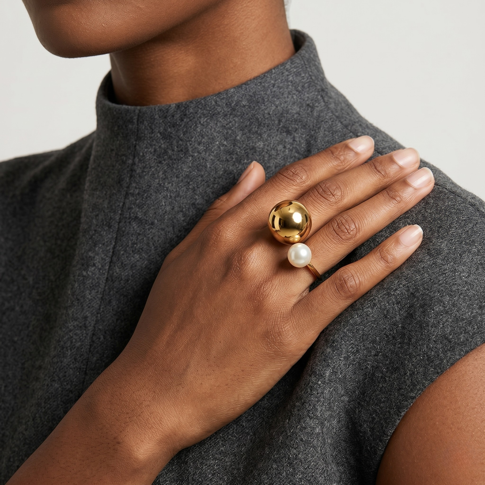 Woman wearing gold and pearl ring on right hand, gray sleeveless top context