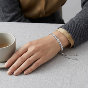 A silver-toned diamond bracelet with dangling chain ends worn on a woman's wrist, shown in a lifestyle setting with a cup of coffee on a table- J.Collins Jewelry