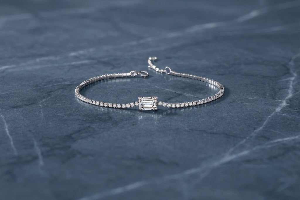 A white gold tennis bracelet with a rectangular baguette-cut center stone, displayed on a dark slate surface - J.Collins Jewelry