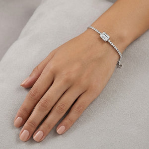 A white gold diamond bracelet with a rectangular baguette-cut center stone, shown worn on a woman's wrist with her hand resting on a light gray textured surface - J.Collins Jewelry