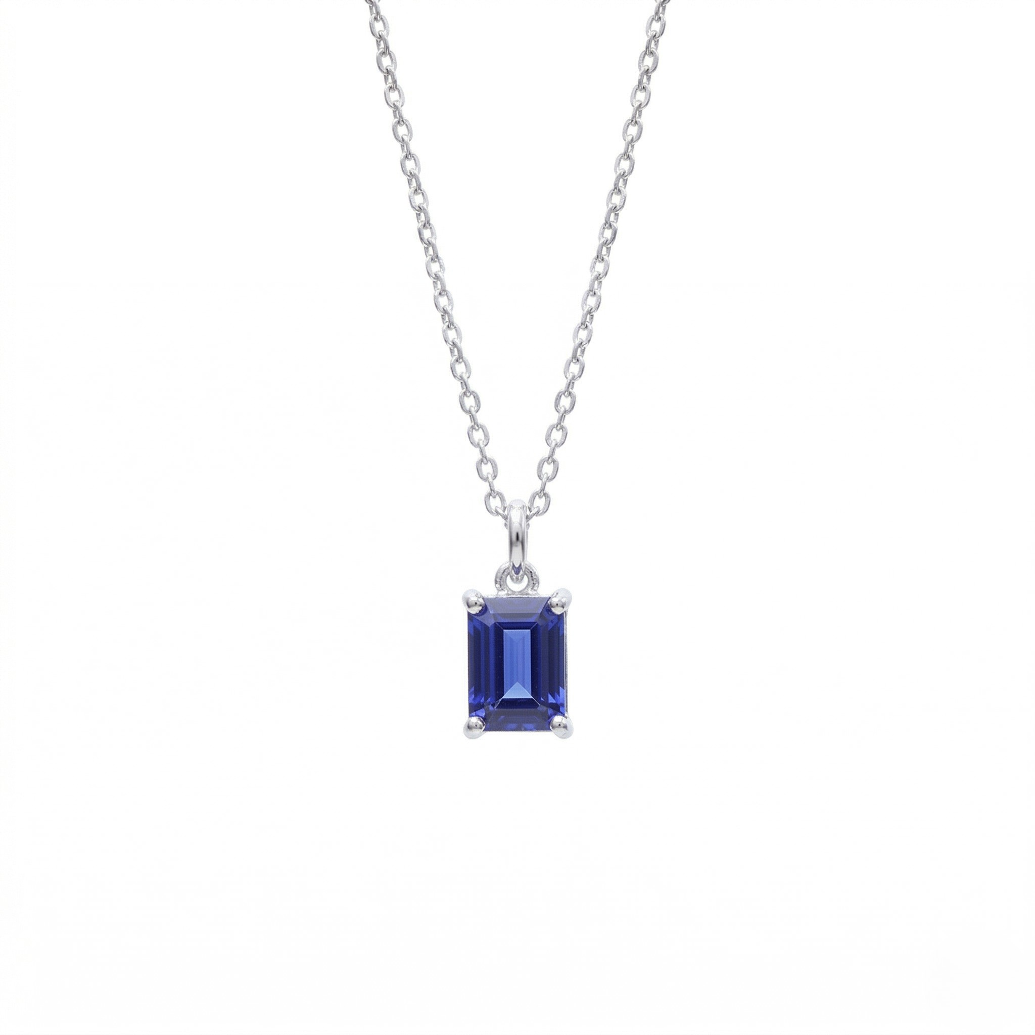 Silver emerald cut blue sapphire solitaire pendant necklace with four-prong setting on silver cable chain, white background - Sapphire Pendant Necklace - J. Collins Jewelry