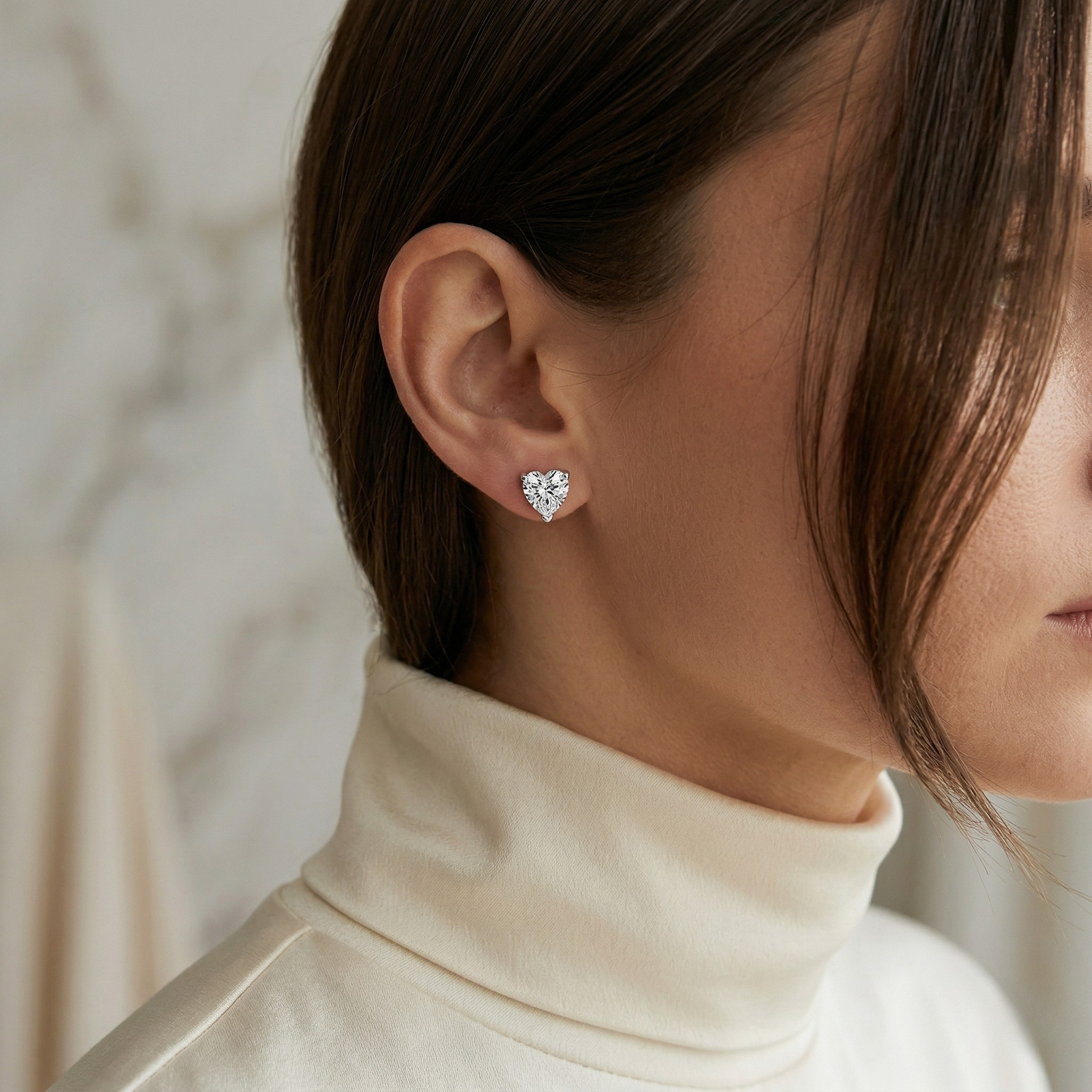 Woman Wearing Silver Heart-Cut Diamond Stud Earrings with White Turtleneck. Silver_Heart_Shaped_Crystal_Stud_Earrings - J. Collins Jewelry 