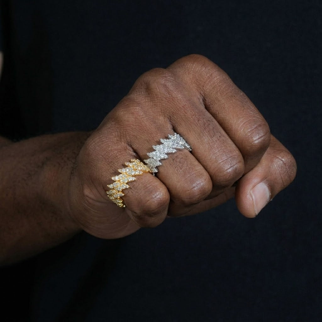 A close-up of a person's hand wearing two textured, diamond-encrusted rings in yellow gold and silver, set against a dark navy background - J.Collins Jwelry
