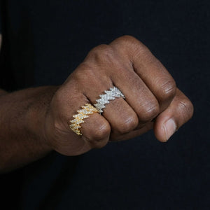 A close-up of a person's hand wearing two textured, diamond-encrusted rings in yellow gold and silver, set against a dark navy background - J.Collins Jwelry