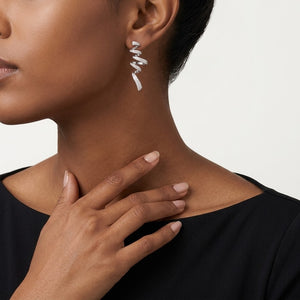 A close-up of a model's neck and ear wearing a single silver spiral drop earring, with her hand resting near her collarbone against a plain light background. J. Collins Jewelry 