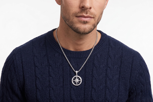 Man wearing a navy cable knit sweater with a silver necklace featuring a compass pendant on a white background-J.Collins Jewelry