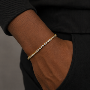 A close-up of a person's wrist wearing a delicate gold tennis bracelet with small clear stones, paired with a black ribbed sweater and black pants - J.Collins Jewelry