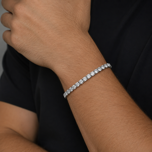 A close-up of a person's wrist wearing a classic tennis bracelet against a black shirt background - J.Collins Jewelry