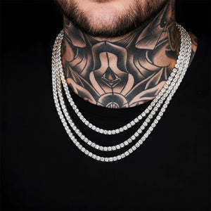 A close-up of a tattooed neck and lower face wearing three layered silver chains set with clear stones against a black shirt and black background - J.Collins Jewelry